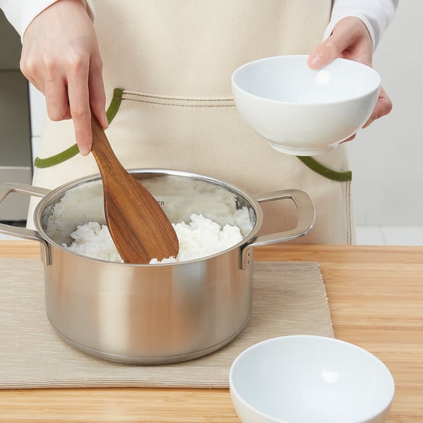 Person serving rice with spoon, apron, bowls nearby.