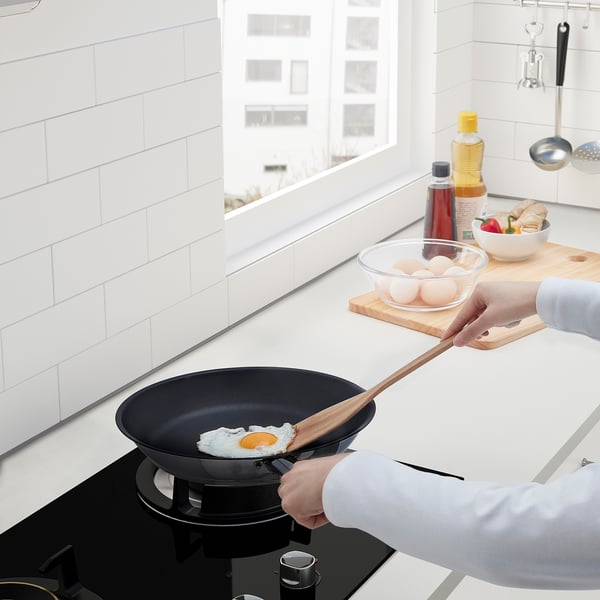 A person is cooking an egg in a non-stick frying pan on a stovetop. Nearby, there are eggs, oil, and other kitchen items.