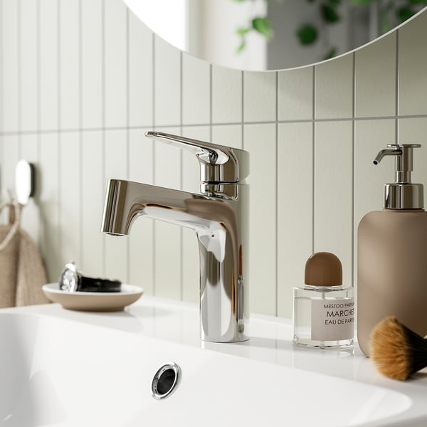 Modern bathroom scene featuring chrome MAJSJÖN tap, small perfume, and make-up tools on a sink with tiled backdrop.