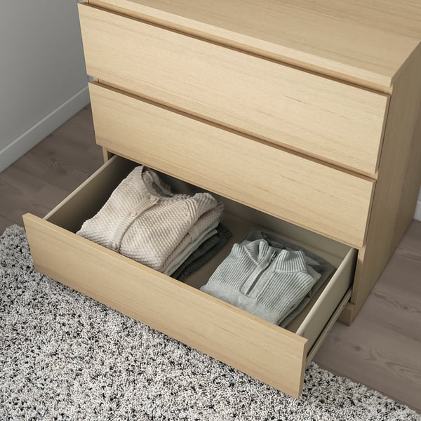 Light wood chest with open drawers revealing neatly folded clothes. Drawers have smooth runners and a stop mechanism.