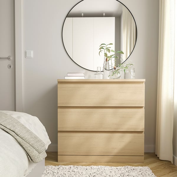 Modern light brown MALM dresser with mirror and plants between bed and door.