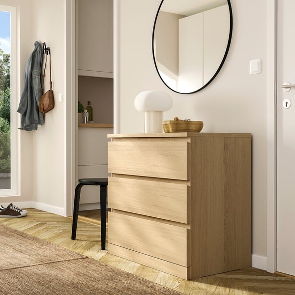 Wooden MALM chest with 3 drawers, lamp, bowl, mirror above, central in room.