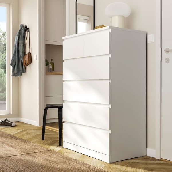 White MALM chest with 6 drawers next to a black stool and mirror. Sits between a door and window, taller than stool.