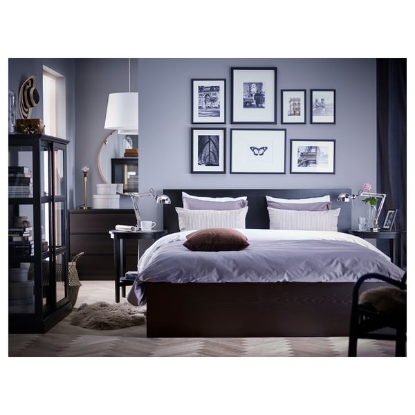 Modern bedroom with a dark MALM bed, light purple bedding, black furniture, and grey walls. Wall decorated with framed artworks.