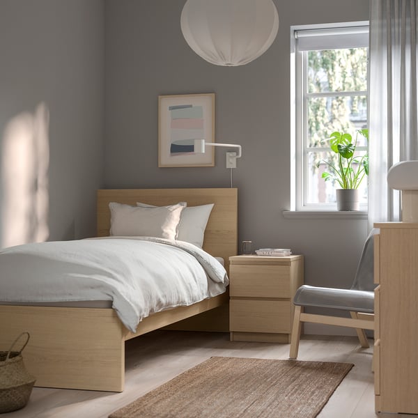 Modern bedroom with light wood MALM bed, abstract art, grey rug & chair by window.