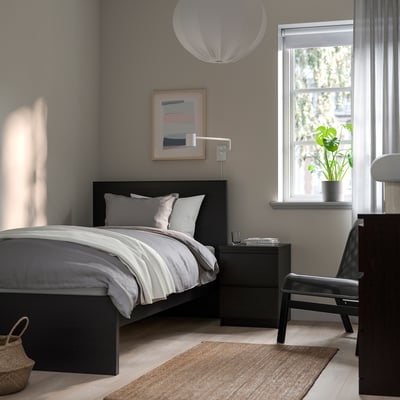 Modern bedroom with black MALM bed, grey linens, bedside table, plant, art, and rug.
