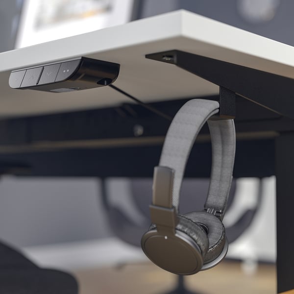 Image shows a modern desk with a built-in controller for height adjustment, featuring hooks for headphones or bags, and a cable management tray.