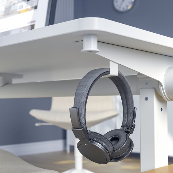 Black headphones hang on white table hook, ideal for meeting rooms.