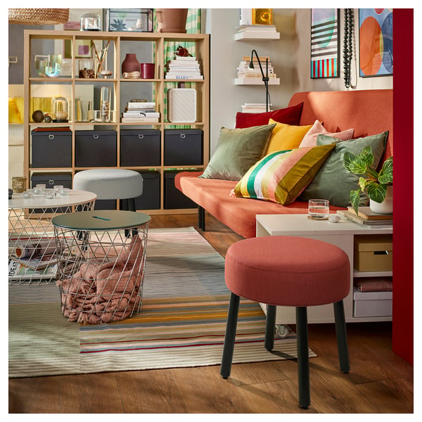 Bright living room with MÖRTFORS pouffes in orange and grey; colourful cushions, shelves with decor, and a striped rug.
