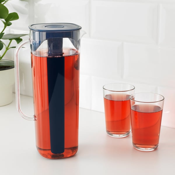Plastic jug with blue handle holds red drink, chills with frozen insert. Two full glasses beside.