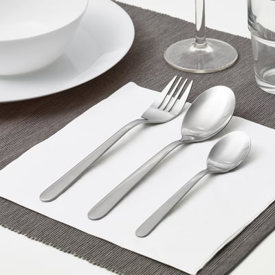 A neatly arranged table setting featuring a fork, spoon, and teaspoon on a napkin, alongside a plate and glass, showcasing everyday cutlery.