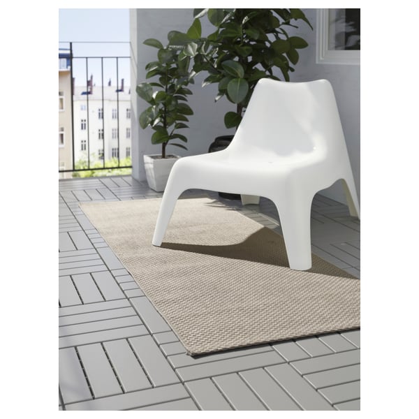A modern balcony with a white chair on a beige rug. The rug is designed for outdoor use, adding warmth and comfort to the space.