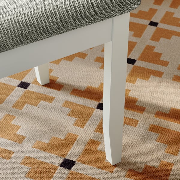 Modern bench with angled legs, embroidered geometric-patterned beige rug.