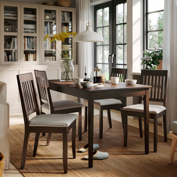 Dark wood dining table with 4 chairs, cushioned seats, flowers, books.