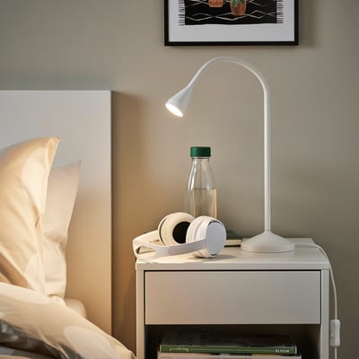 Minimalist bedroom with NÄVLINGE lamp, book, headphones, and water bottle on bedside table, cosy atmosphere.