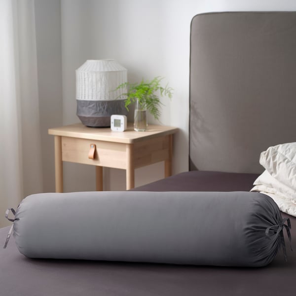 Grey cylinder pillow on bed, ties at ends, against headboard.