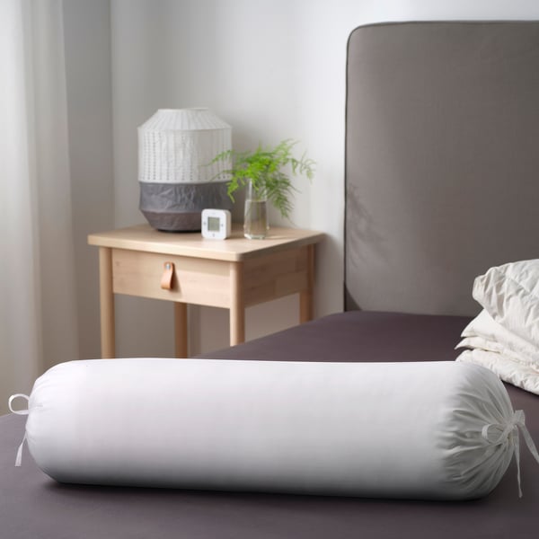 Bedroom with NATTJASMIN pillow on bed, bedside table with lamp, plant, clock.