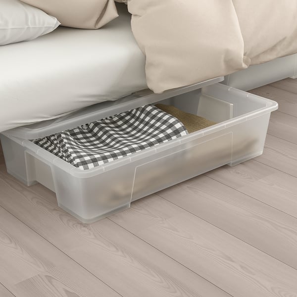Clear storage box under bed holding chequered blanket, showcasing space-saving function.