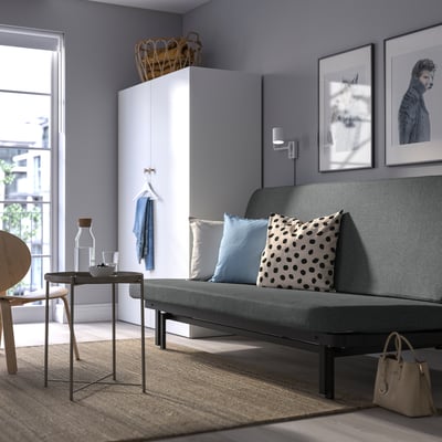 Modern living room with NYHAMN grey sofa-bed, white cabinet, stylish decor, and natural light from large window.