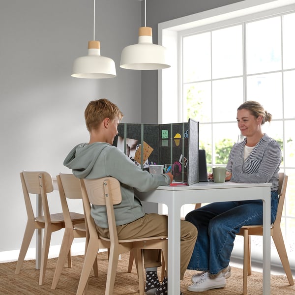 Two people sit at a table with a desk divider for privacy and focus. The divider has storage and pockets, aiding concentration.