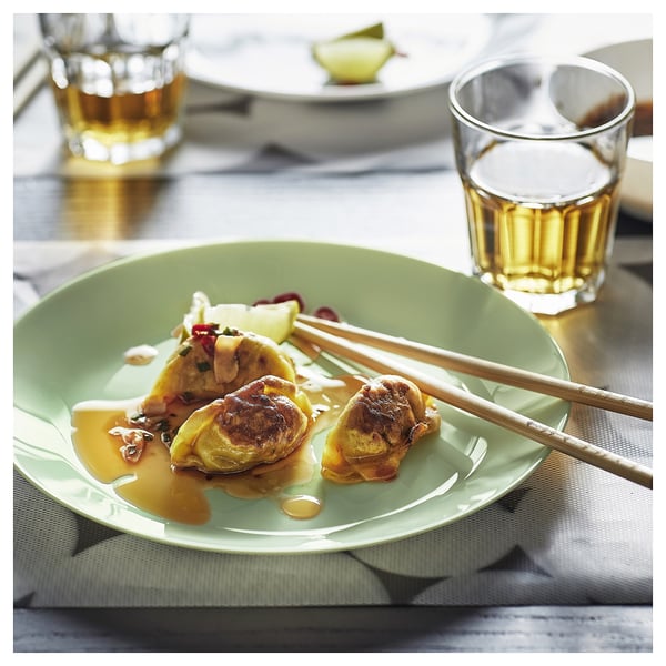 A green glass plate with fried food and chopsticks, next to a glass of amber liquid.