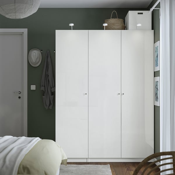Modern bedroom with large white PAX wardrobe against dark green wall. Wardrobe is taller than bed and door, with clean lines and minimalist design.