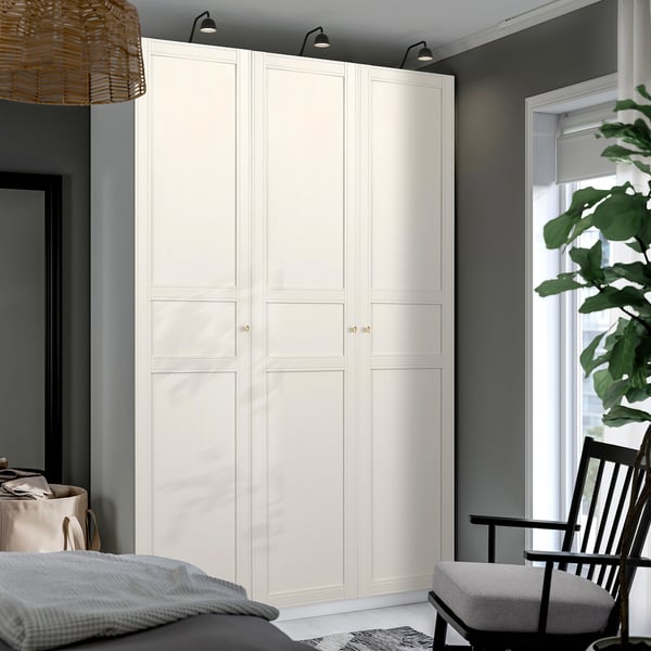 Minimalist bedroom with large white PAX wardrobe, sleek design, tall and wide, grey walls, modern chair, bed, and plant.