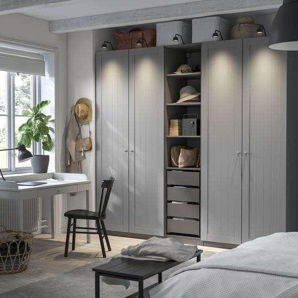 Modern bedroom with grey PAX wardrobe, integrated lighting, and storage. Beside bed: lamp, plant, hats, bags.