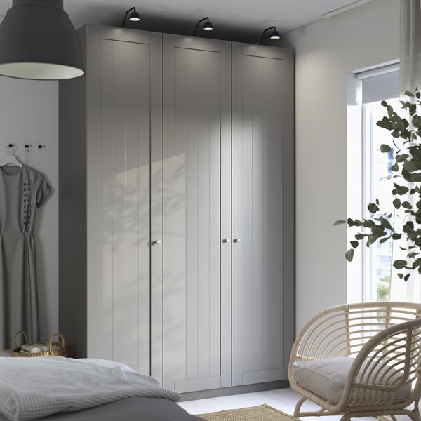 Modern bedroom with tall gray ikea PAX wardrobe, lighting, dark lamp, garment, wicker baskets, wicker chair, window, minimal decor.