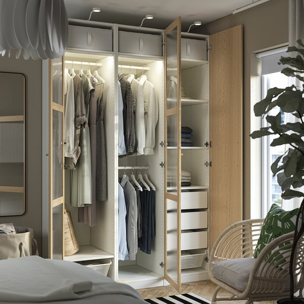 Open wardrobe displaying clothes, with integrated lighting and shelves. It includes hanging space, drawers, and a mesh basket for storage.