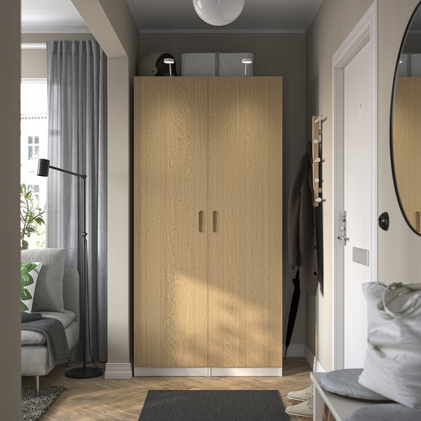 Modern entryway with tall light wood PAX wardrobe, grey curtains, and coat stand beside white door.