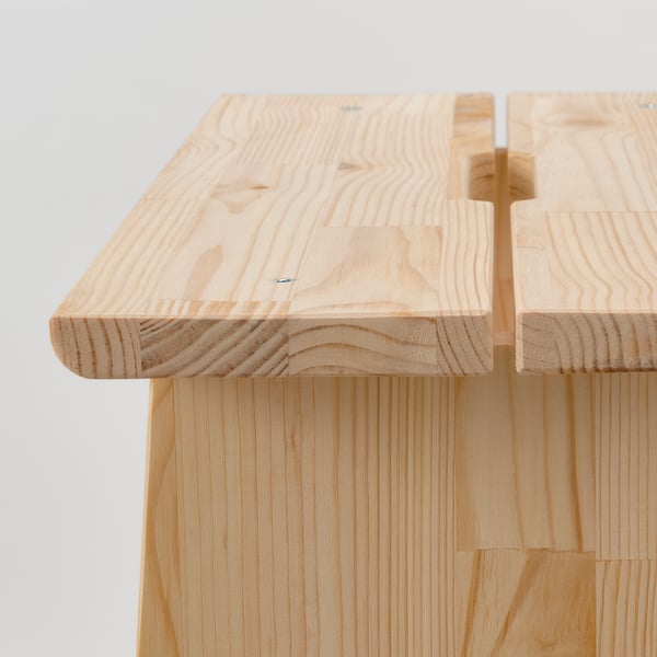 Smooth pine wood stool with rounded edges and handles, made of light-colored planks.