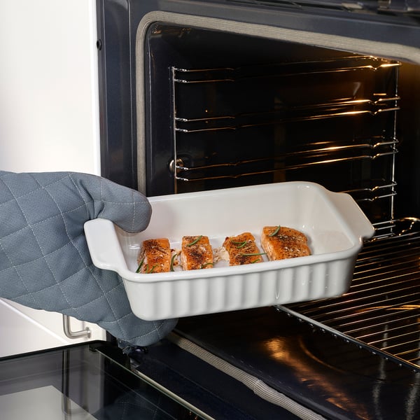 Person holding white oven dish with seasoned salmon fillets, ready to bake.