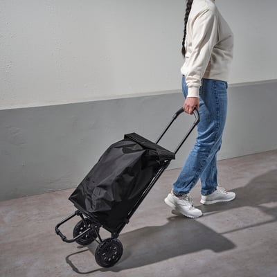 A person pulls a black RADARBULLE bag on wheels; adjustable handle, holds items securely.