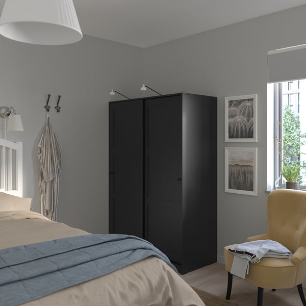 Modern grey RAKKESTAD wardrobe in bedroom with yellow chair, blue quilt, wall hooks, and large window.
