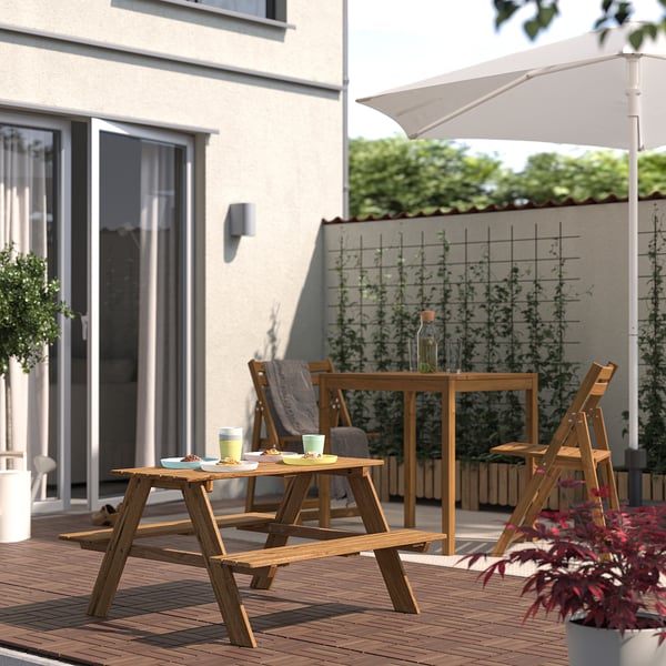 Small wooden RESÖ kids picnic table set on deck, next to larger furniture. White umbrella provides shade.