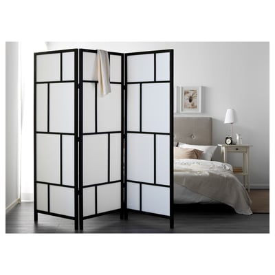 Black & white pine RISÖR room divider with grid design, larger than bed & bedside table, draped with cloth.