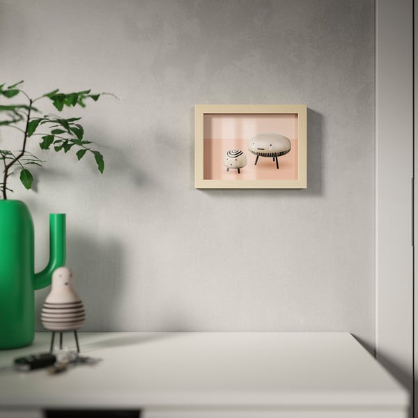 A picture frame with two stools on a grey wall, and a green vase with a plant on a white table below.