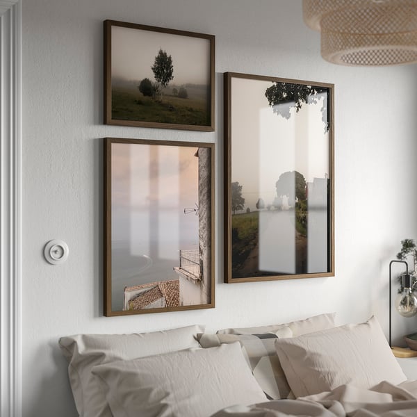 Three light wooden frames above bed: two landscape, one vertical.