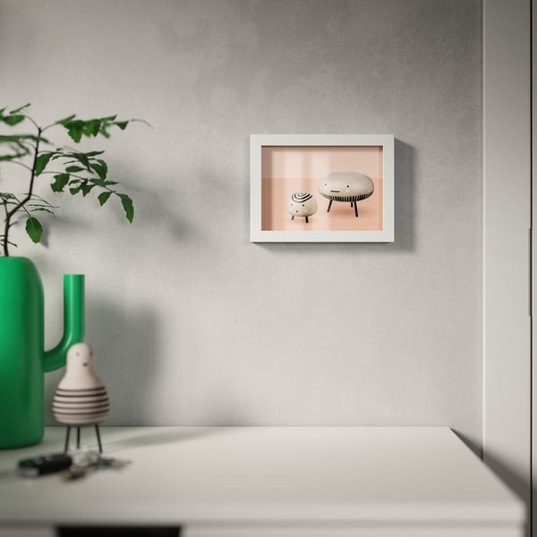 Wall frame with two white objects, near plant and decor.