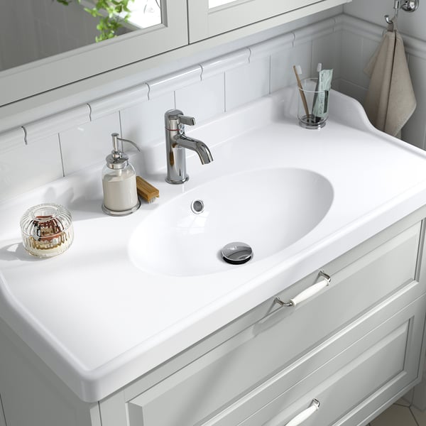 Beautiful white bathroom sink with chrome tap, soap dispenser, and toothbrush holder, set in a classic white vanity cabinet.
