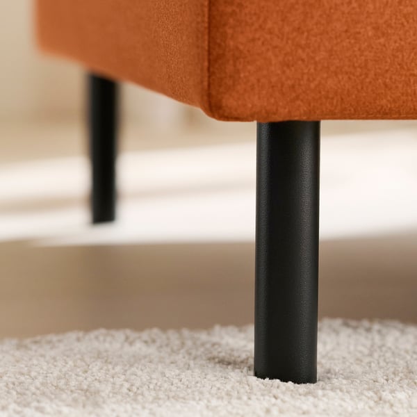 Modern orange sofa with sturdy black metal legs, shown on plush white carpet.