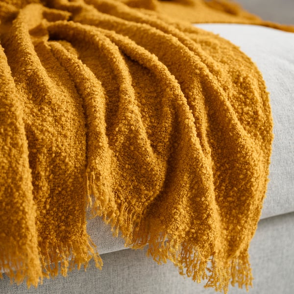 Mustard yellow, cosy throw blanket with textured surface draped over a cushion.