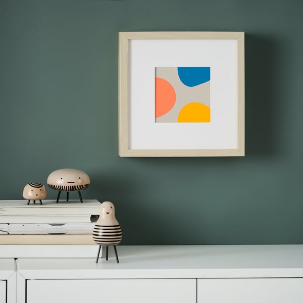 A teal wall displays a framed image with colourful shapes. Below, a table holds stacked papers and ceramic figurines.