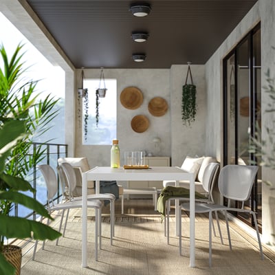Modern patio with SEGERÖN table & stackable chairs. Minimalist, weather-resistant. Glass door, wall art, hanging plants.