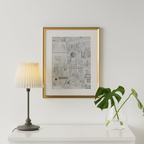 Framed ticket collage on wall, between lamp and plant, gold finish.