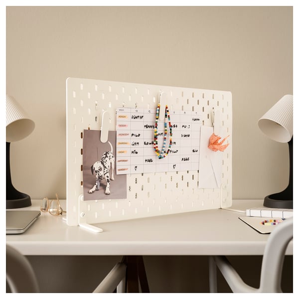 Organised workspace with SKÅDIS white pegboard displaying calendar and notes, flanked by lamps on either side.