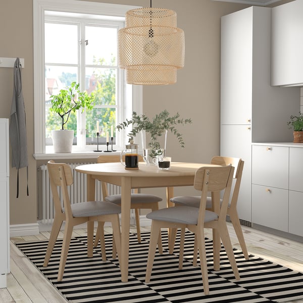 Light wood dining set with 4 chairs, striped rug, hanging lamp, near window.