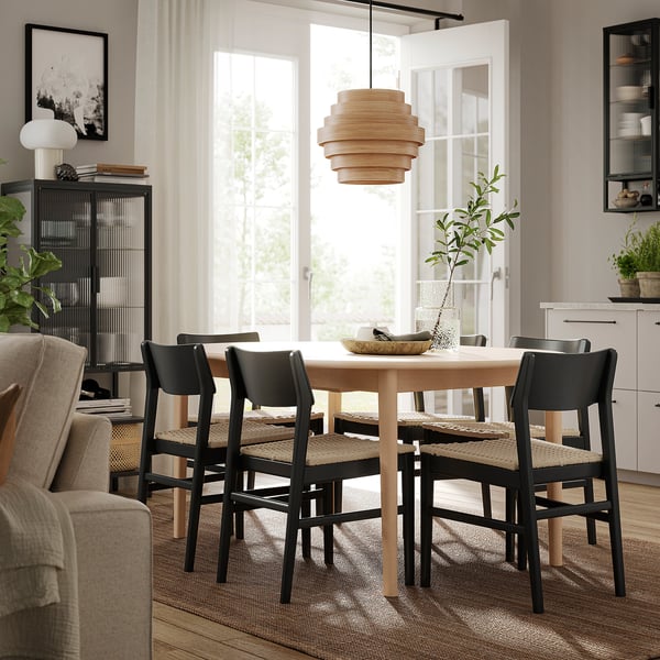 A cosy dining area with a light wood SKANSNÄS extendable table, black chairs, and a stylish pendant light.