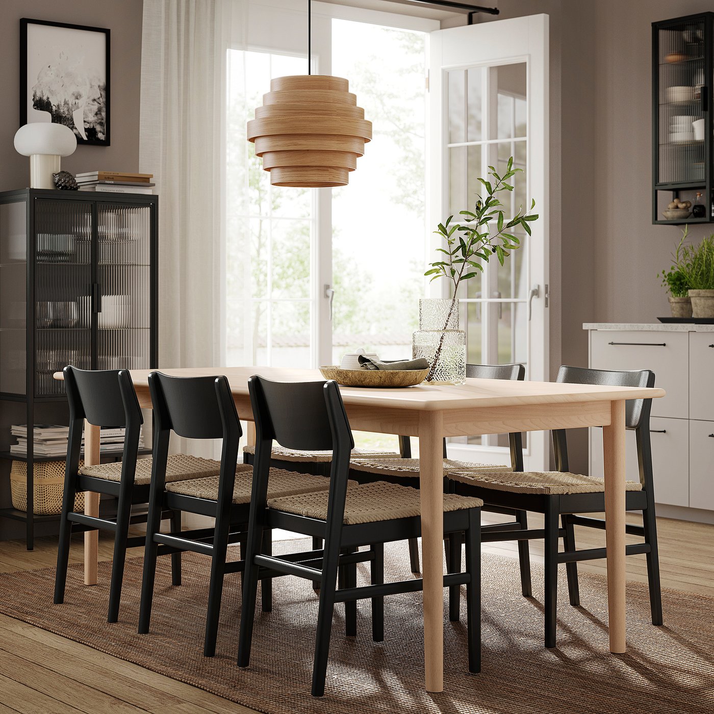 Modern dining area with light wood table, four black chairs with woven seats, hanging wooden lamp, and large window.